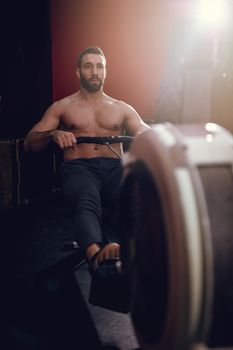 A handsome man pulling the rowing machine in the gym. 