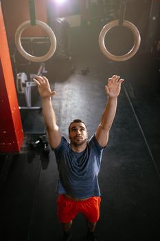 Young muscular man is preparing to do exercise on gymnast rings at the gym.
