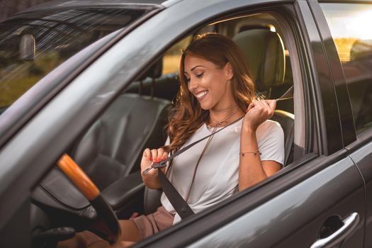 Beautiful business woman sitting on car seat and fastening seat belt.