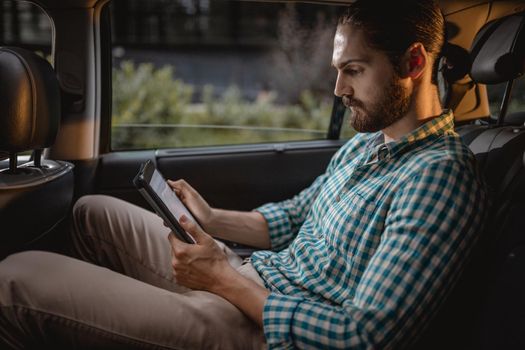 Young confident businessman is working on a business trip on the back seat in car.