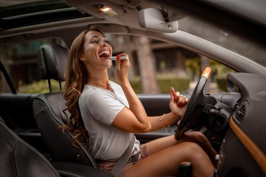 Young attractive woman looking in rear view mirror painting her lips doing applying make up in the car.
