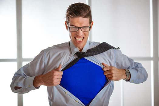 Angry businessman ripping open his shirt and exposing a superhero blue costume underneath. Looking at camera.