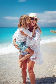 Beautiful little boy enjoying with his mother on the beach. She is embracing him and he is kissing mother's cheek.