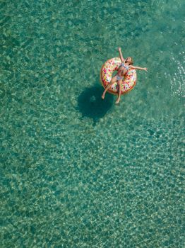 Aerial view of little girl swimming on the inflatable big donut in the transparent turquoise sea. Top view from drone.
