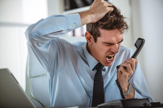 Executive businessman holding an earphone, surprised by bad news he just heard. He is yelling at the phone.