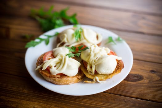 fried in batter sandwiches with tomatoes and mozzarella in a plate with herbs, on a wooden table.
