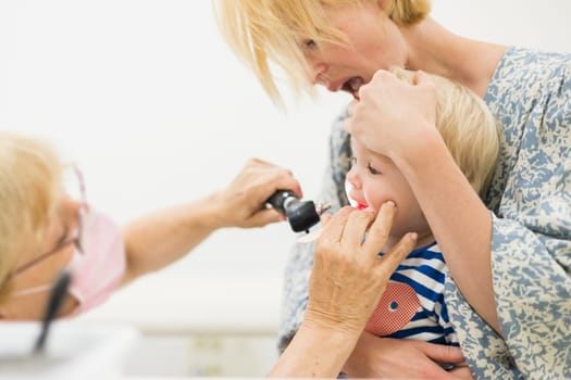 Infant baby boy child being examined by his pediatrician doctor during a standard medical checkup in presence and comfort of his mother. National public health and childs care care koncept