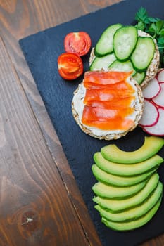 Crispy sandwich with red fish. Snacks Bread and fitness food. Rice bread and avocado, parsley, cherry tomatoes on a dark background.