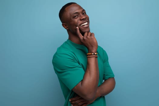 shy young american man in a t-shirt holds his hand to his face on a blue background with copy space. people lifestyle concept.