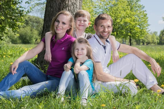 Father, mother and their children are sitting on the green grass in the summer park