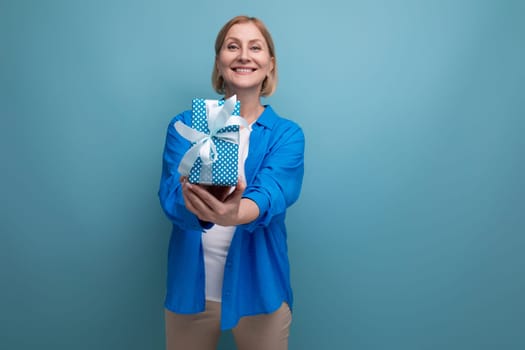 mature woman giving gift for holiday on blue background copy space.