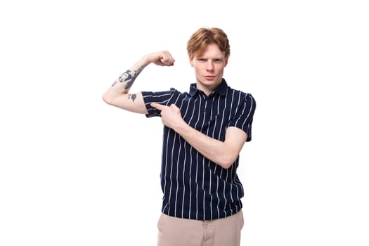 confident young European blond guy in a striped polo shirt shows his tattoos on a white background.