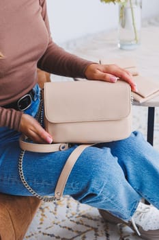 A beautiful woman holds a beige leather bag in her hands. A small women's cocktail bag.