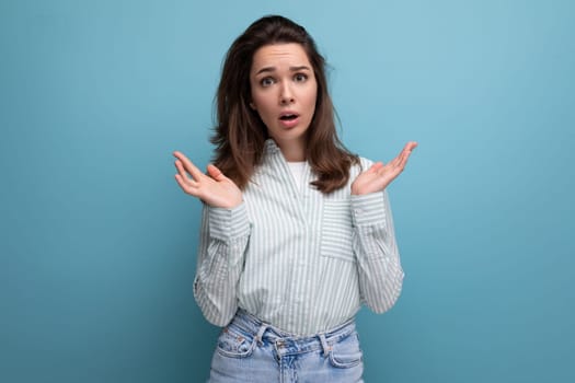 upset young brunette female adult in striped shirt and jeans on studio background.