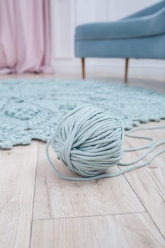 Handmade carpet knitted from natural threads, flooring, natural cotton. Beige handmade carpet. Knitted decorative item. Skein of blue knitting thread