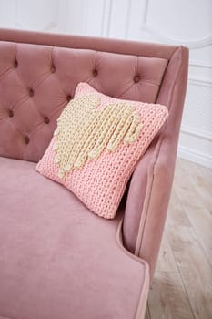 Knitted handmade pillow with pink threads lies on the sofa.