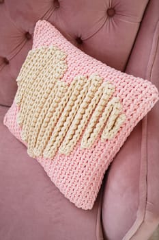 Knitted handmade pillow with pink threads lies on the sofa.