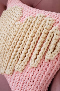 Knitted handmade pillow with pink threads lies on the sofa.