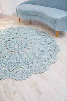 In a bright room on the floor there is a round blue handmade carpet. flooring, natural cotton. Blue knitted handmade carpet on the floor