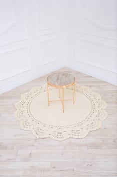 A knitted cotton rug and a decorative round table lie on the floor against the backdrop of the interior. Handwork. Beige handmade carpet.