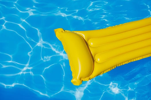 A yellow air mattress floats in an empty pool of blue water. Summer holiday concept