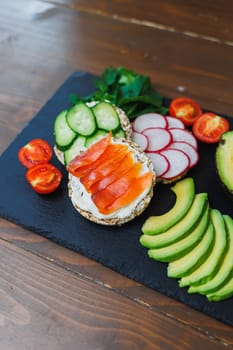 Crispy sandwich with red fish. Snacks Bread and fitness food. Rice bread and avocado, parsley, cherry tomatoes on a dark background.