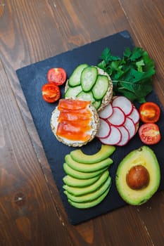 Crispy sandwich with red fish. Snacks Bread and fitness food. Rice bread and avocado, parsley, cherry tomatoes on a dark background.