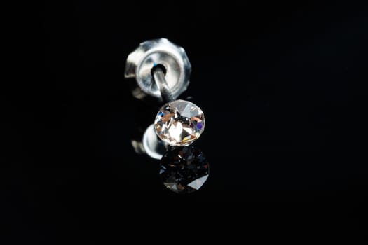 Silver earring macro photo with a precious stone on a black isolated background. Selective focus.