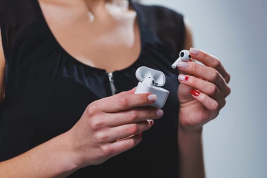 White wireless headphones in a woman's hand, close-up. Headset with charging case.
