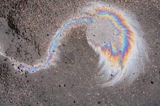 Rain blurred car oil from a malfunctioning car in a parking lot. Texture of asphalt and rainbow stains. Environmental pollution concept