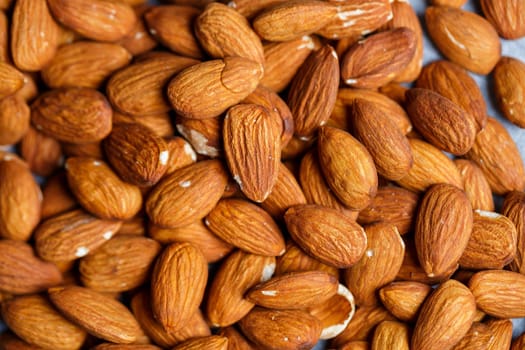 Delicious roasted sweet almonds lie in a large heap, nuts close-up.