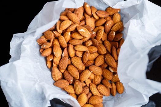 Delicious roasted sweet almonds lie in a large heap, nuts close-up.