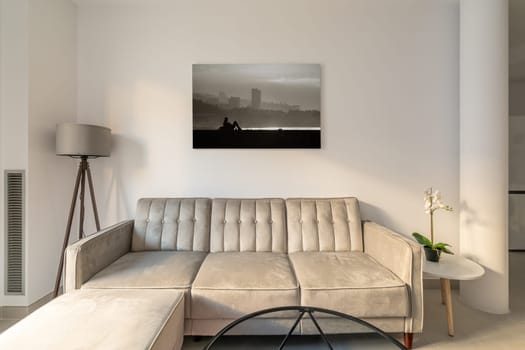 Comfortable beige corner sofa near a glass coffee table on a picture in a cozy living room. Concept of a lounge zone for meeting guests or relaxing after work.