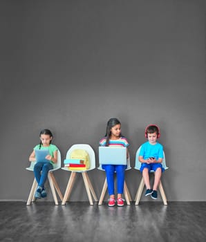 Growing up with wireless gadgets. Studio shot of kids sitting on chairs and using wireless technology against a gray background