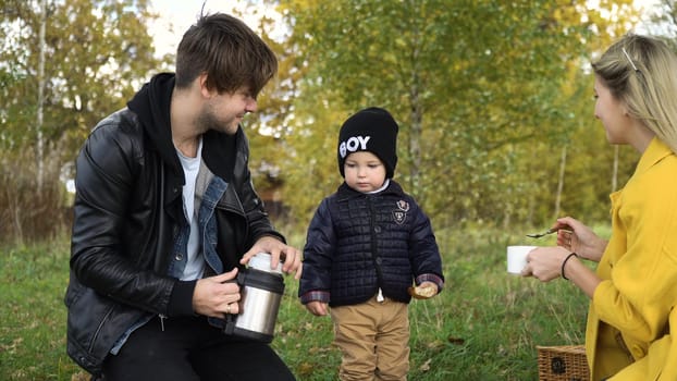 Young family with son at a picnic in the park on a sunny day. Family having picnic outdoors. Young smiling family doing a picnic on an autumns day. Family picnicking together.