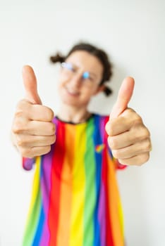 Close-up portrait of a pretty cheerful flirtatious girl in a bright striped t-shirt, LGBT flag, showing a double ok, like sign