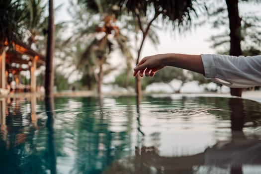 The graceful touch of a woman's hand on the turquoise water surface creates ripples, symbolizing the harmonious bond between humans and nature.