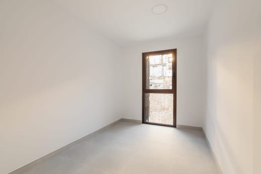 Narrow empty room with a panoramic door-window overlooking the sunny summer cityscape. The concept of the apartment after the delivery of a new building or renovation.