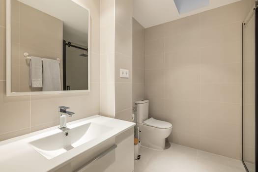 Stylish spacious bathroom with toilet, shower and sink with cabinet and mirror in beige tones in a new building. Concept of convenient and concise renovation in the bathroom. Copyspace.