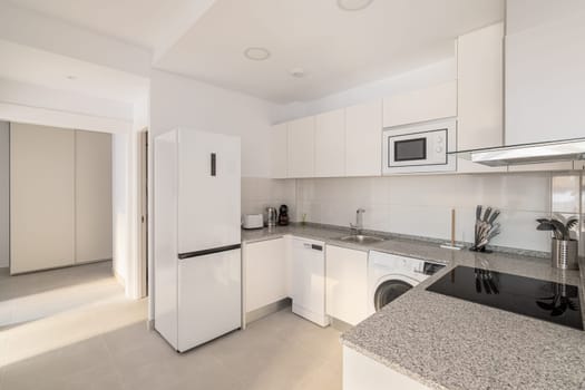 White stylish kitchen with modern appliances refrigerator washing machine and stove for cooking. Concept of a comfortable multifunctional kitchen after renovation.