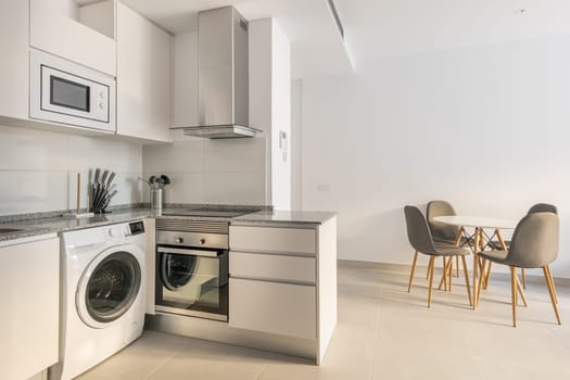 Comfortable bright kitchen with modern appliances refrigerator, washing machine and stove for cooking and a table with chairs. The concept of a multifunctional living room kitchen.