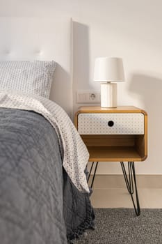 Close-up of a bedroom with a double bed and a wooden bedside table in light colors and a lamp. The concept of a stylish comfortable bedroom for a young family.