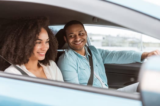 Automobile ride. Loving young arab man and woman sitting inside new car, having summer auto trip to countryside, driver smiling to his wife. Selective focus, side view shot
