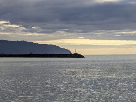 Waialua Bay exudes tranquility as the mountains cast their majestic reflection upon its serene waters, under a moody sky at dusk on the picturesque island of Oahu, Hawaii.