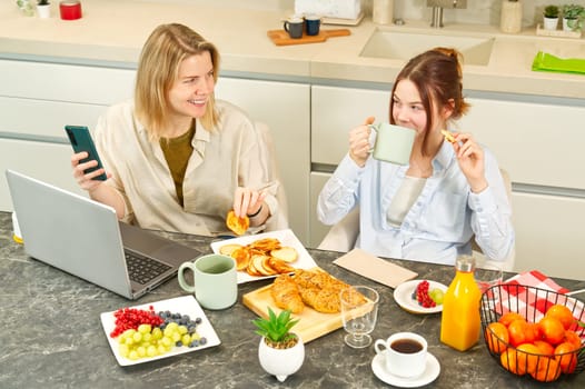 Happy mother and daughter having breakfast in kitchen and using digital devices. Lifestyle, Morning breakfast, mother and daughter together.