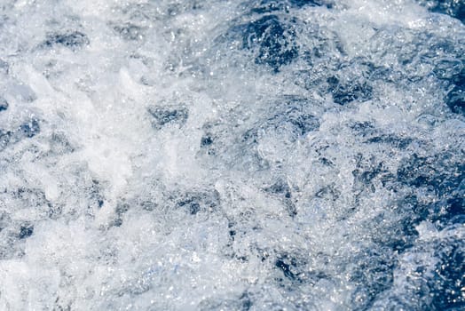 Abstract blue sea water with white waves. Blue sea texture with waves and foam. Rough deep turquoise and blue Mediterranean sea. Sea water top view.