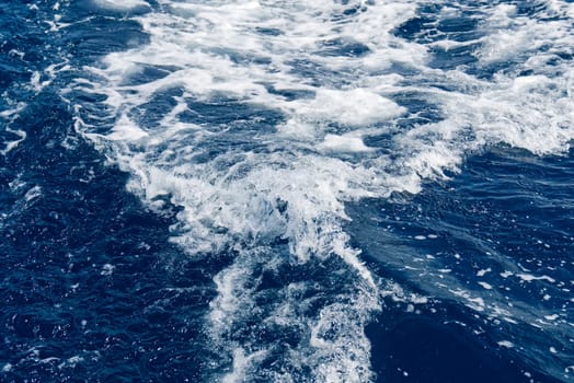 Abstract blue sea water with white waves. Blue sea texture with waves and foam. Rough deep turquoise and blue Mediterranean sea. Sea water top view.