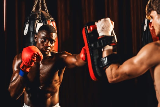 African American Black boxer punching at trainer or coach wearing punching mitts as boxing bag training equipment in the gym. Strength and stamina training for professional boxing match. Impetus