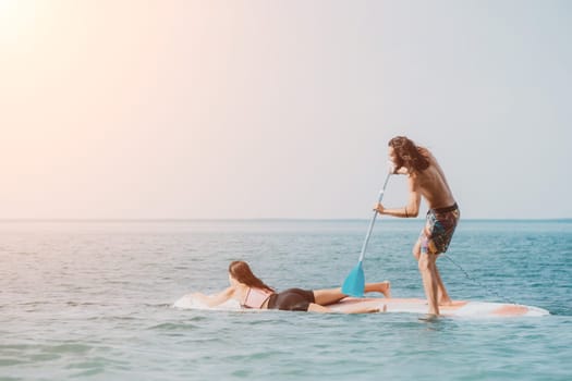 Sea woman and man on sup. Silhouette of happy young woman and man, surfing on SUP board, confident paddling through water surface. Idyllic sunset. Active lifestyle at sea or river