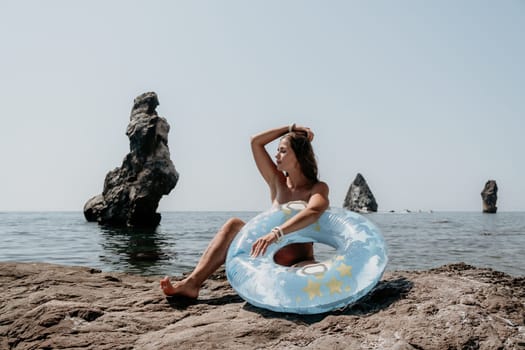 Woman summer sea. Happy woman swimming with inflatable donut on the beach in summer sunny day, surrounded by volcanic mountains. Summer vacation concept